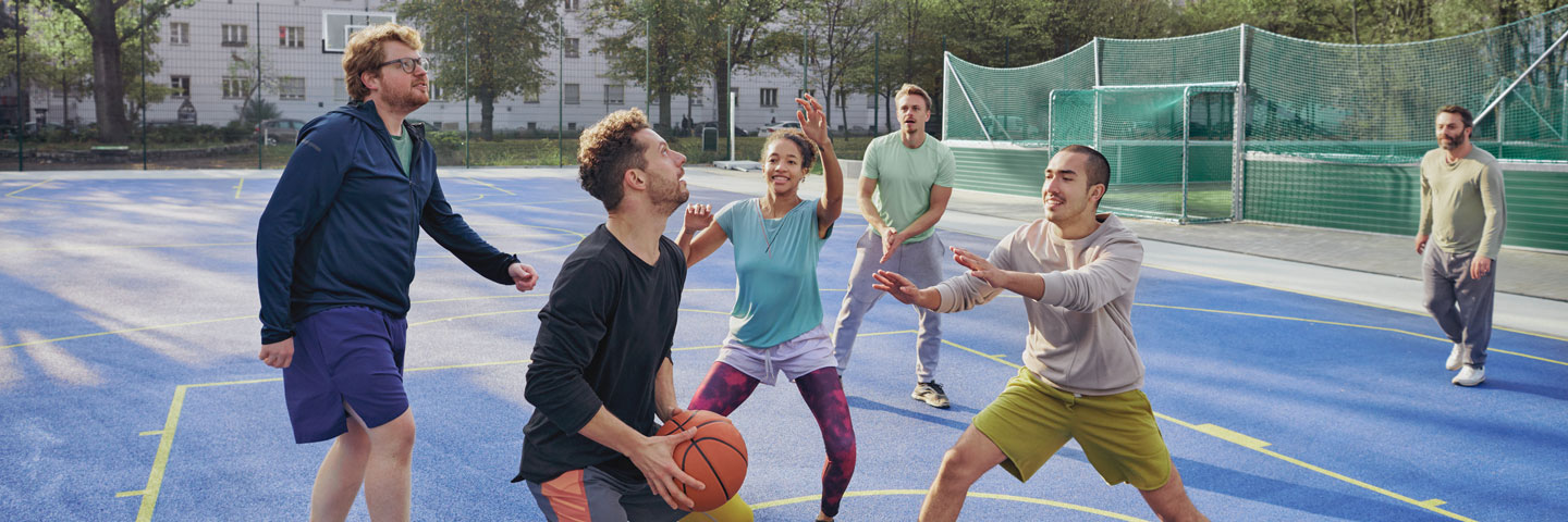 Praxisbeispiele Betrieblicher Gesundheitsförderung Freizeitsport auf dem Sportplatz, sechs Menschen spielen Basketball auf einem Sportplatz.