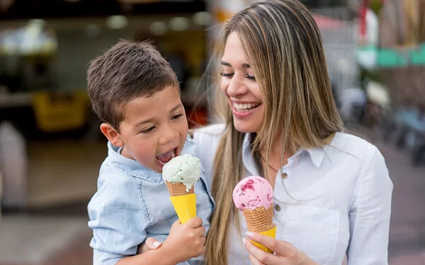 Eis aus der Eisdiele: Eine Mutter hat ihren Sohn auf dem Arm, beide essen eine Kugel in der Waffel.