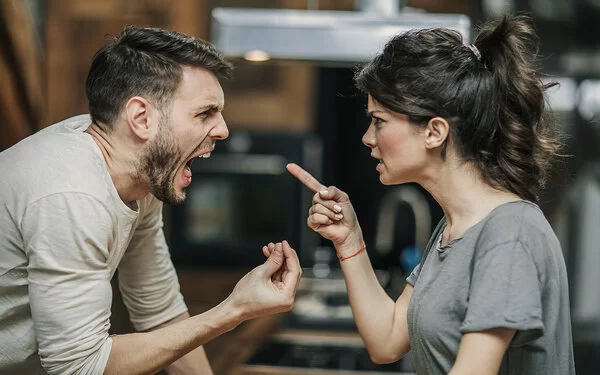 Ein Paar steht sich gegenüber. Beide streiten miteinander und sind sehr wütend. Die Frau richtet den Zeigefinger auf ihren Partner. Der Mann hat den Mund weit geöffnet und schreit. Mit den Fingern der rechten Hand macht er eine Drohgebärde.