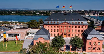 Landtag RLP Außeansicht Foto zeigt den Blick auf das historische rotbraune Gebäude im Hintergrund fließt der Rhein