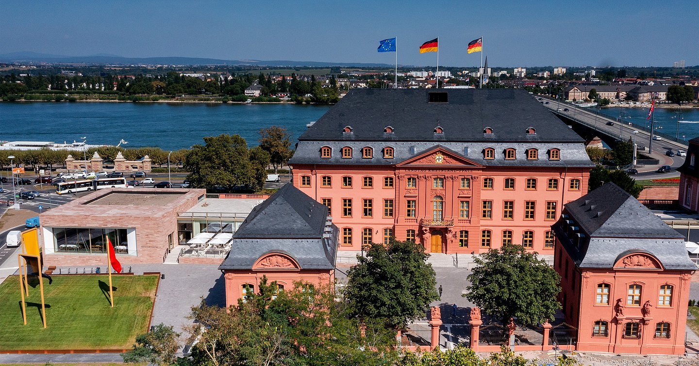 Foto zeigt den Blick auf das historische rotbraune Gebäude im Hintergrund fließt der Rhein